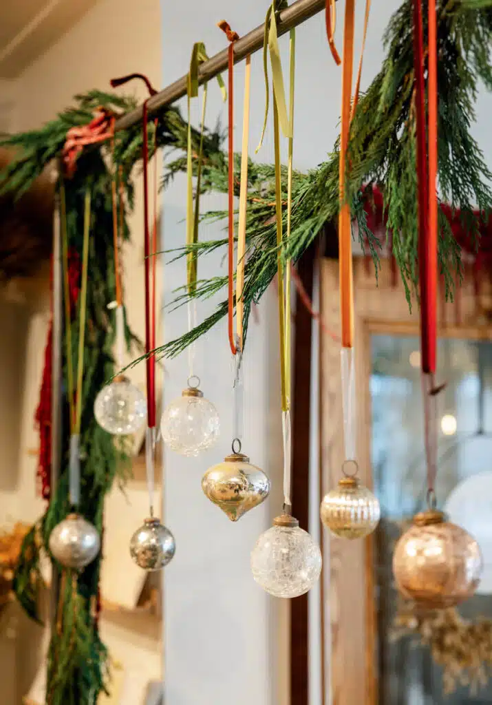 Glass Christmas ornaments hanging from a metal rod decorated with evergreen boughs.