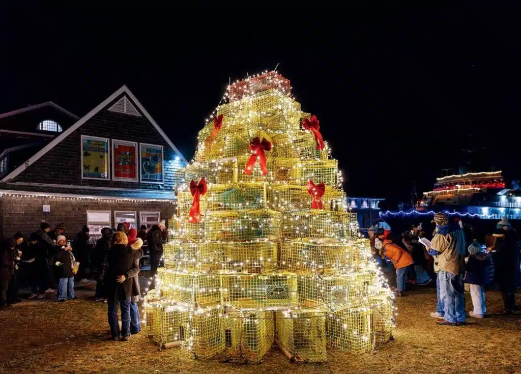 A Christmas tree made of stacked, illuminated lobster traps in front of a building at night.