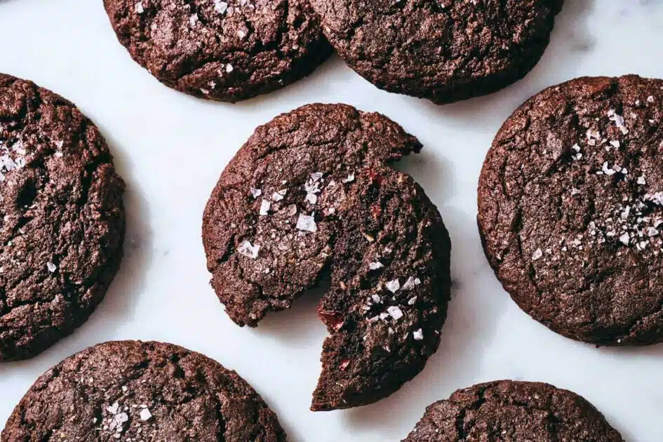 Gluten-Free Chocolate-Coconut Buckwheat Cookies. Five chocolate cookies topped with sea salt, one of which is broken in half.