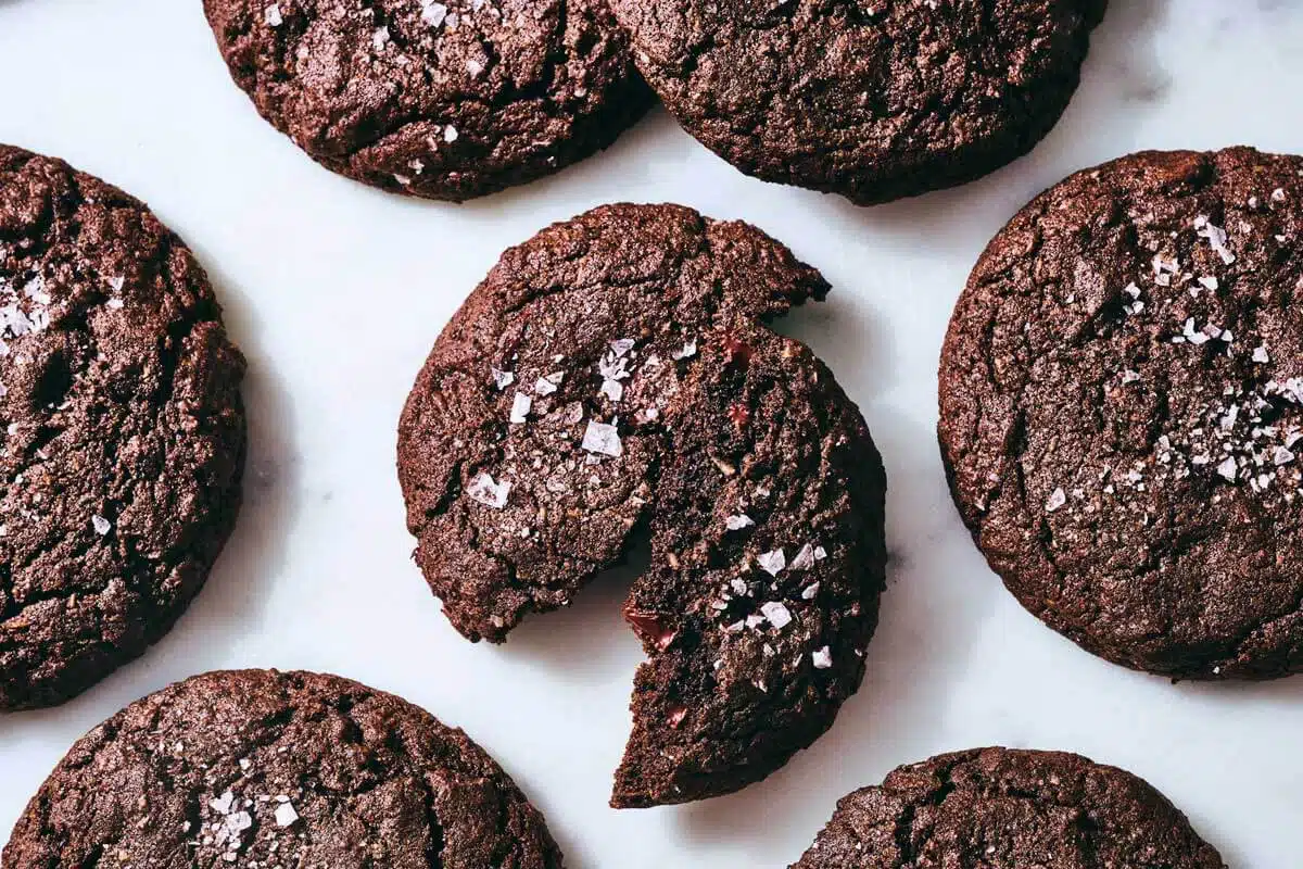 Gluten-Free Chocolate-Coconut Buckwheat Cookies. Five chocolate cookies topped with sea salt, one of which is broken in half.