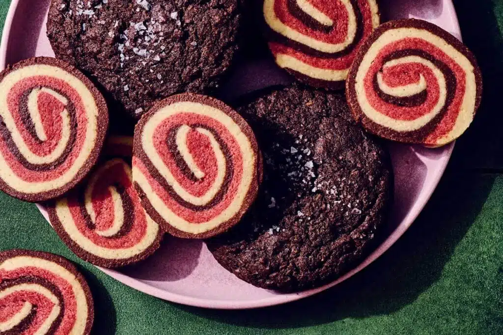 A pink plate holding red and yellow pinwheel cookies and dark chocolate cookies sprinkled with sea salt.