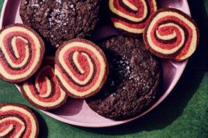 A pink plate holding red and yellow pinwheel cookies and dark chocolate cookies sprinkled with sea salt.