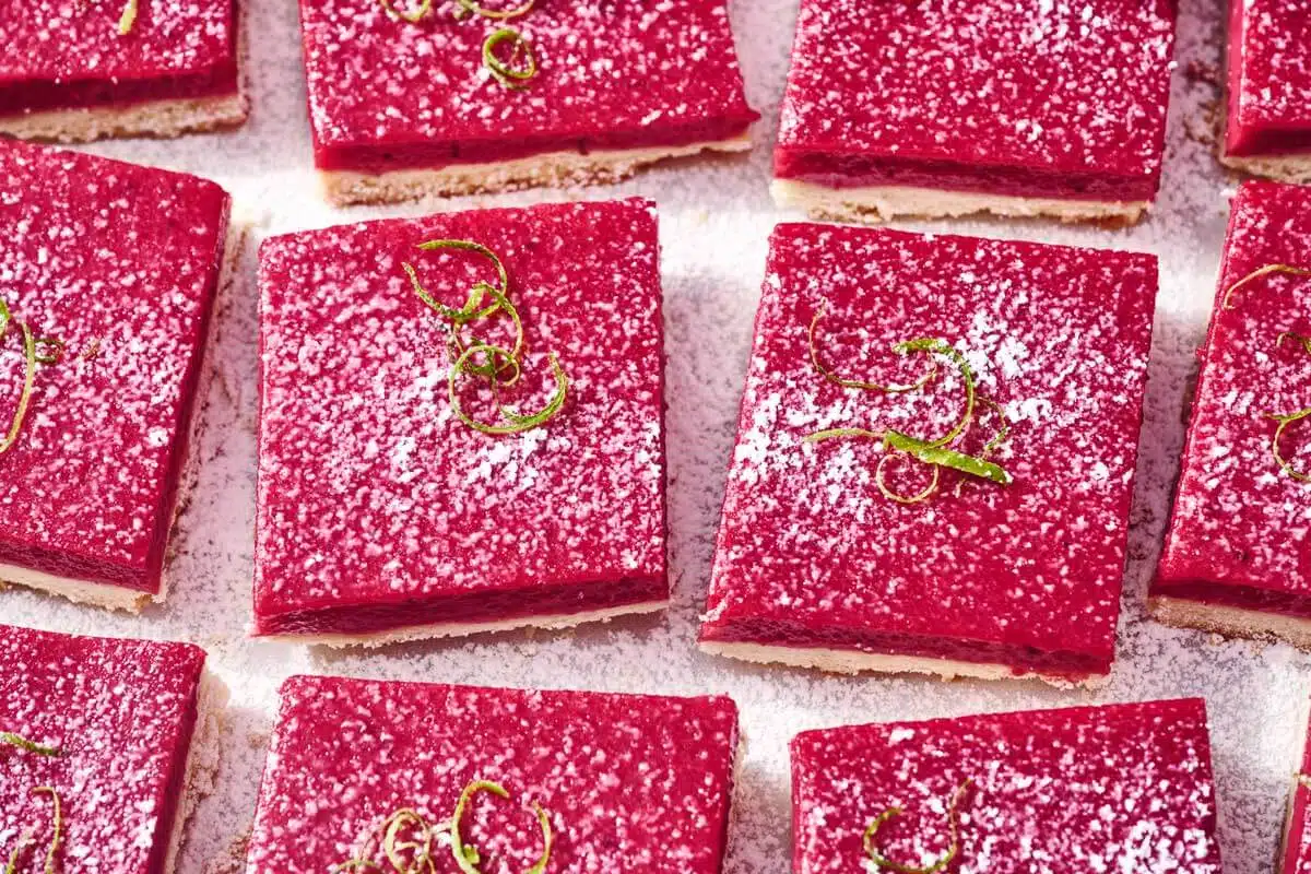Cranberry-Lime Bars. Square slices of bright pink berry bars topped with powdered sugar and lime zest.