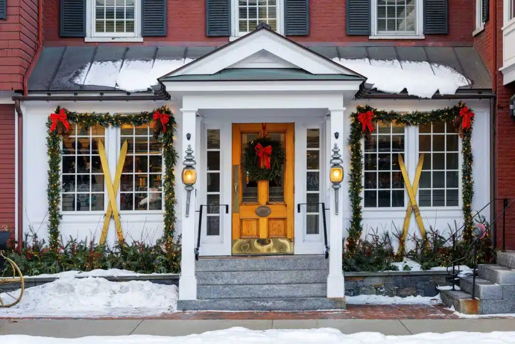 The front entrance of a brick building decorated for the holidays with wreaths, garlands, and crossed wooden skis.