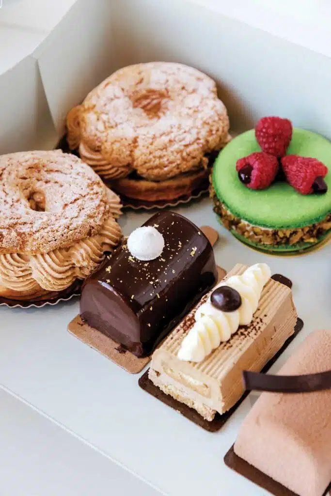 A box of assorted pastries, including cream puffs, a green macaron with raspberries, and chocolate cakes.