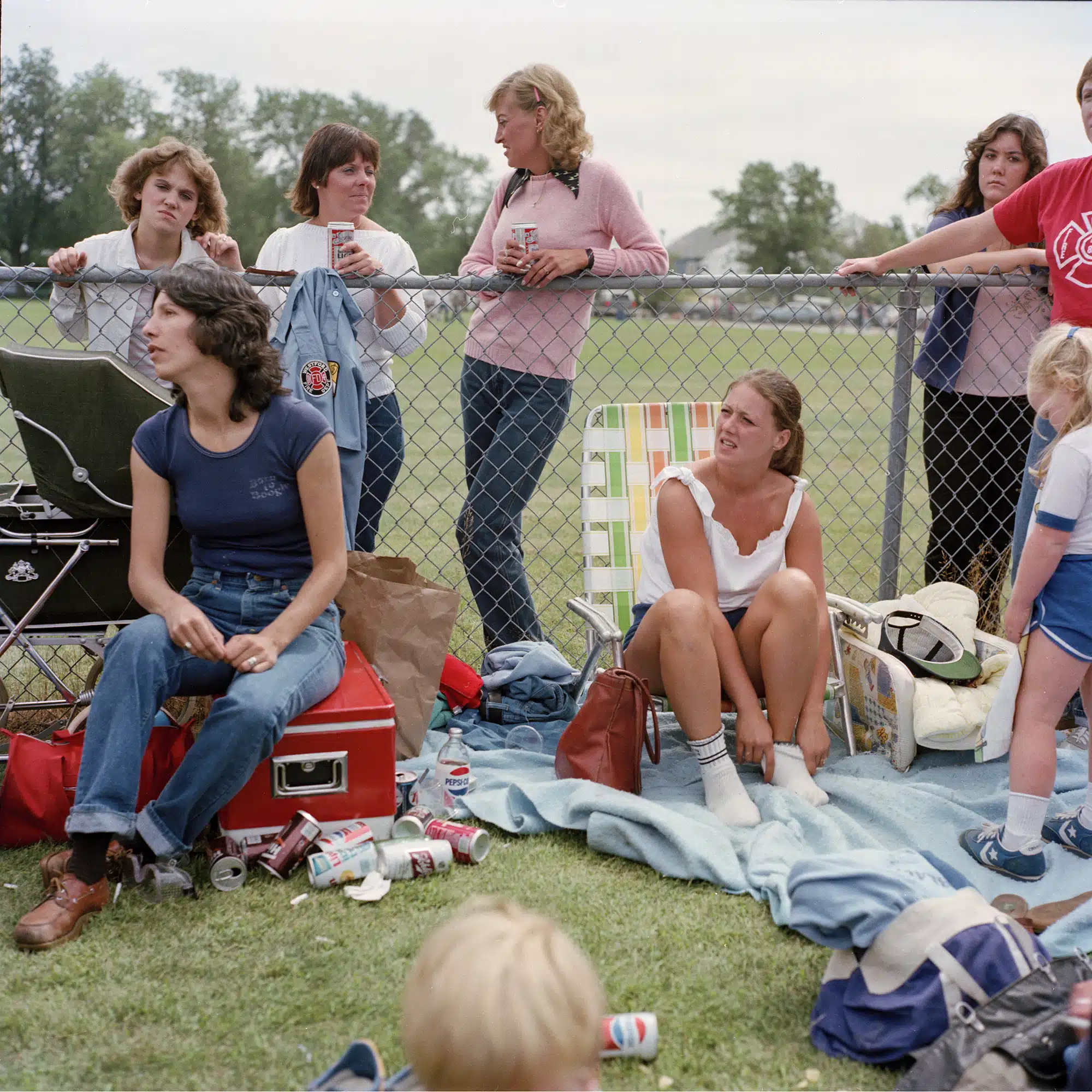 Ball Field - 1983 "This photo was taken at a little league baseball game. What I find particularly interesting besides the fact that they are overtly drinking beer in a public place, that if this photo was taken today everyone here would be on their cell phones. Either, using them to take photos or using them to chat or on the web etc. I feel that if you look at the photos from this non technological era you will see people are lost in thought or day dreaming. I love that esp the two woman on the left - they look somewhat pained and lost in thought."