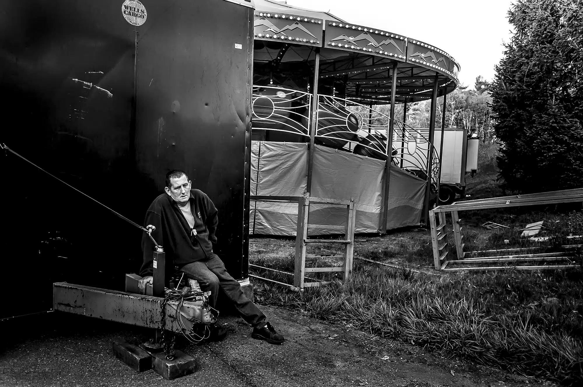 Carnival Break - 2012 "Every year I photographed the Apple Blossom festival since 1982. Each year I look for something different. There is a carnival that goes along with the parade that sets up for three days. I tried unsuccessfully several times to get permission to photograph the workers behind the scenes. As I was walking down a long hill to the carnival I saw this gentleman resting behind a ride. I could see the potential of what appeared to be a perfectly composed photograph, all I had to do put the frame where I needed it and pray he didn’t move– there was a beautiful symmetry to all the lines and the gesture of his body and the weary look on his face. I took one shot. I chatted with him after and he said he was very tired but quite honored to have his photograph taken. When I look at it now I am bit mesmerized by how all the pieces of this little moment fit together perfectly. I also realize that I am the one who is honored to have been given this moment to tell his story."