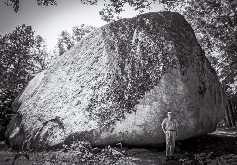 Friends of the Madison Boulder president Brian Fowler at the ancient slab, which not only towers over him but also extends another 10 to 12 feet underground.