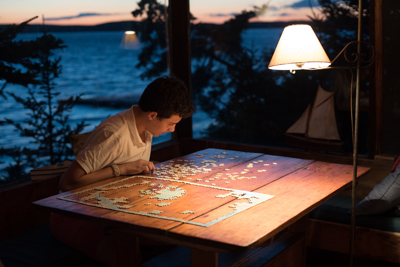 Title: Puzzle Master Location: Little Deer Island, ME. Judge's comments: "The artist’s intent is one way we know the meaning of an art object. The viewer can provide meaning as well, based on personal context. Does this photograph evoke a memory, a feeling or an experience for you? It does for me. The lighting, the puzzle object, the lake as backdrop and the wood tone of the table stimulate a carefree feeling of warmth and memories of summers spent on vacation with my family." 