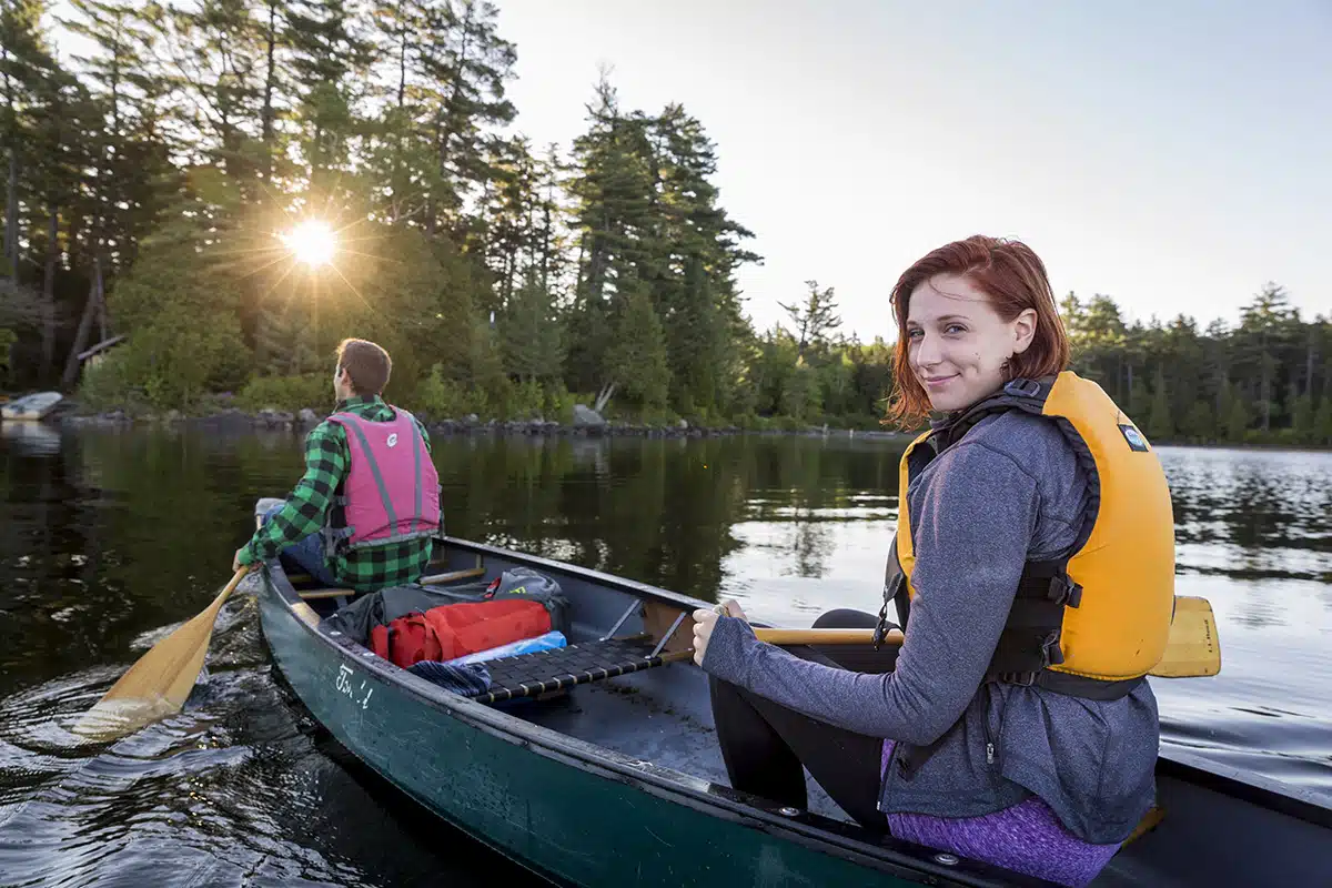 A young couple paddles a canoe on Long Pond in Maine's north woods. At the Appalachian Mountain Club's Gorman Chairback Lodge. Near Greenville, Maine.