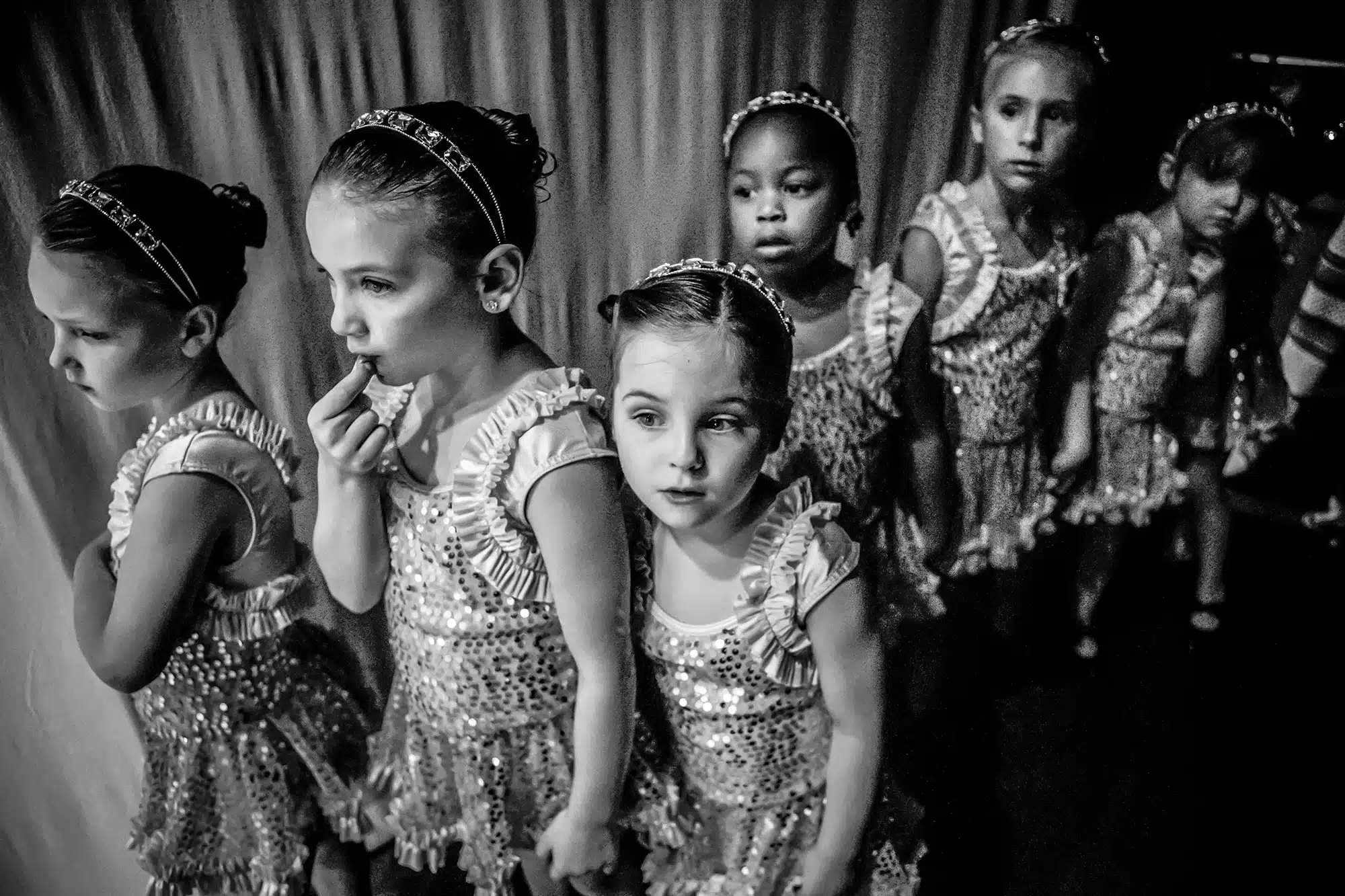 Dance Recital - 2015 "I took ballet for years as a young girl and I have a fondness for dance. My friend had a dance studio and I used to photograph her students for her. I had a standing invitation to come photograph 'behind the scenes' for my project and as it turned out I went in 2015 when my friend was retiring so it was the last recital. I found the most interesting spot was right behind the curtains where the next group of dancers waited to go on stage. The young girls were so curious and of course anxious. Once I was there for awhile they no longer noticed me which was exactly what I wanted."