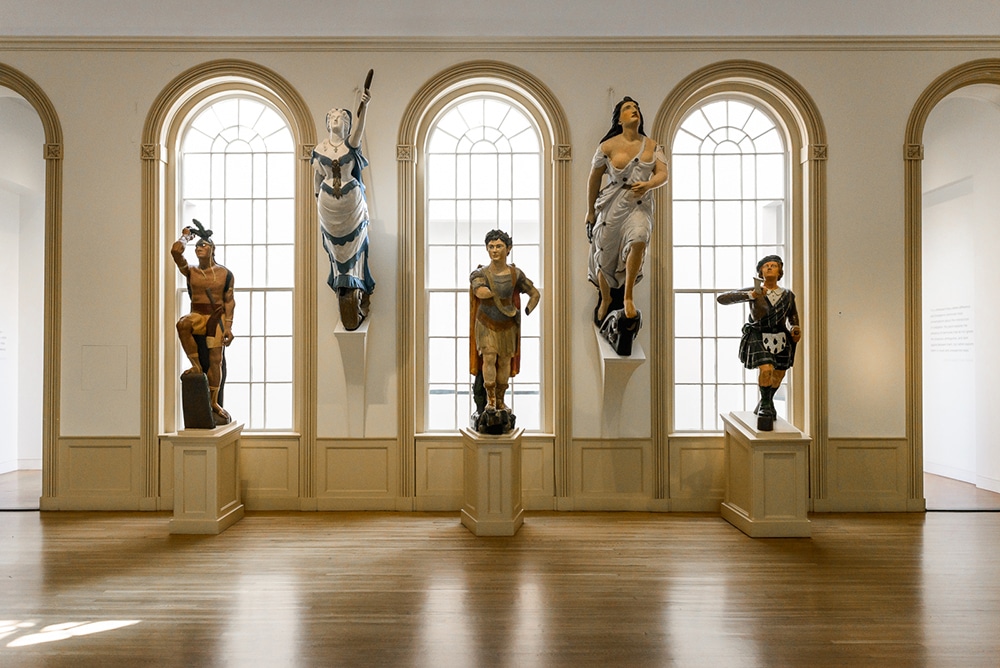 Collection of figureheads, antique wooden figures that originally adorned the prow of sailing ships, displayed in the East India Marine Hall at the Peabody Essex Museum.