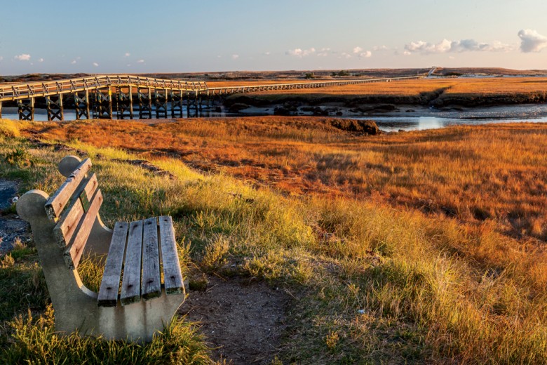 A bench provides a sunrise view of Cape Cod marshland at the Sandwich Boardwalk over Mill Creek.