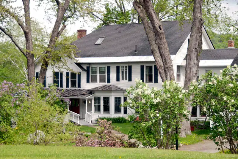 Large white house with black shutters surrounded by trees and blooming bushes on a grassy lawn; New England inns for spring