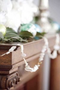 A wooden mantelpiece decorated with a white garland and green ornaments, close-up view.