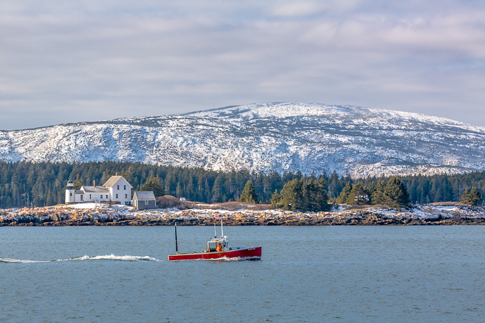 A lobster boat works the waters around Winter Harbor Light near the cliffs in Acadia National Park.