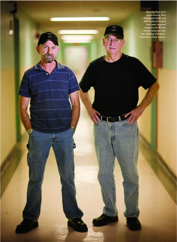 Two men wearing black caps and casual clothes stand in a hallway with their hands on their hips, facing the camera. A caption next to them provides additional context.